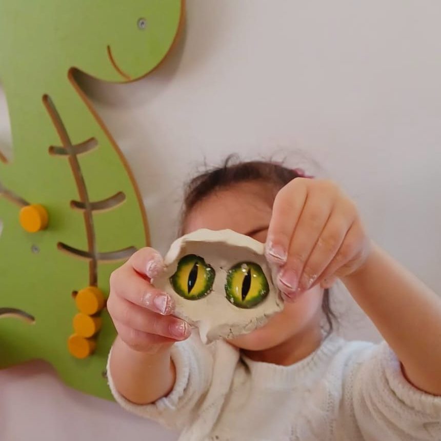 Ein Kind hält mit stilisierten reptilienartigen Augen vesehenes Knetstück in die Kamera.