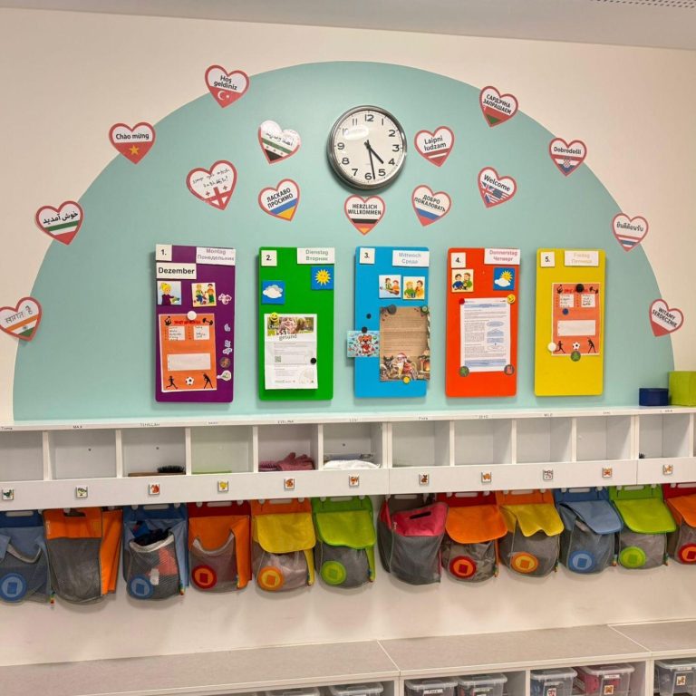 Wand mit einer Uhr, farbigen Tafeln und Ablagefächern in einer Kinderumgebung.