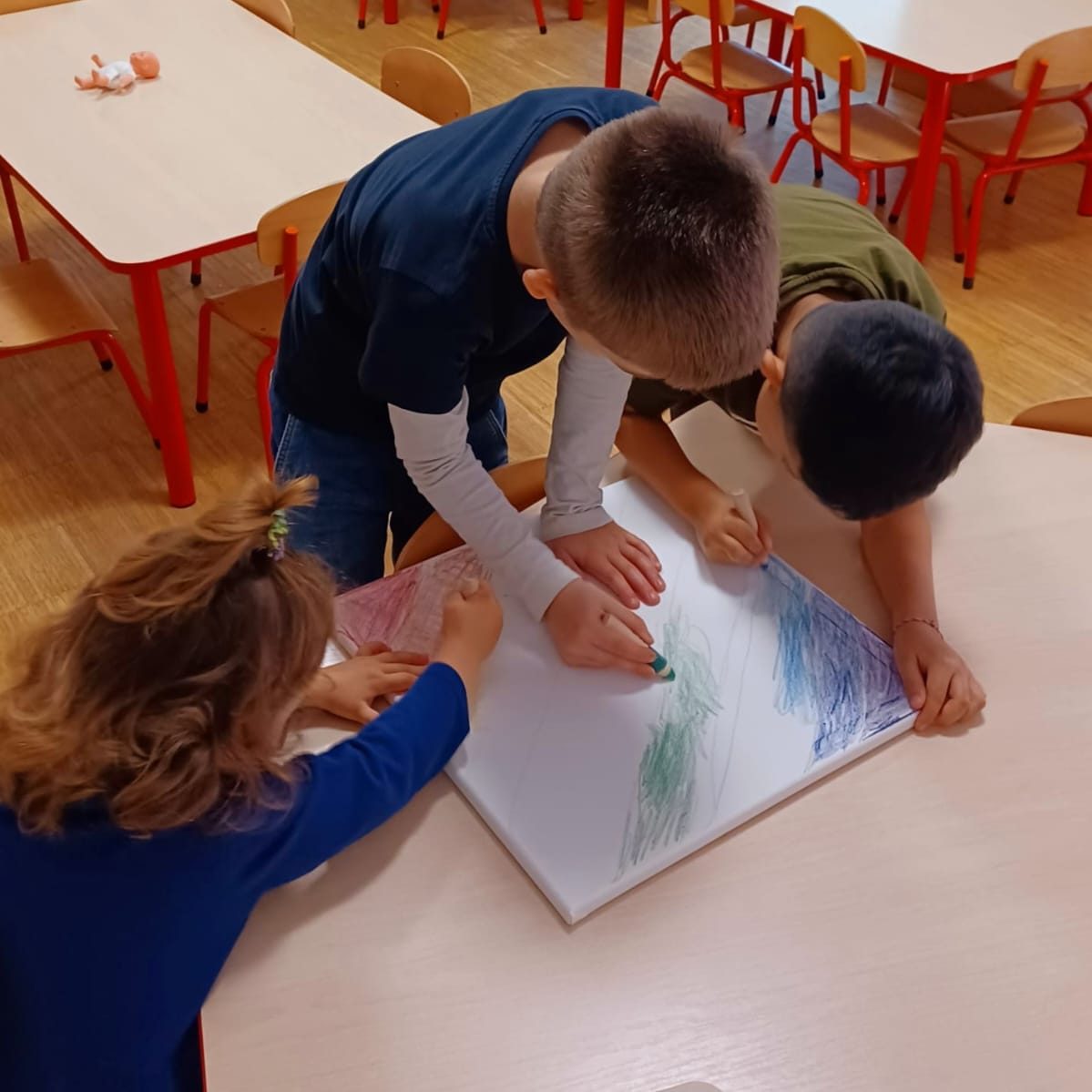 Drei Kinder zeichnen gemeinsam mit Buntstiften auf einem großen Blatt Papier.