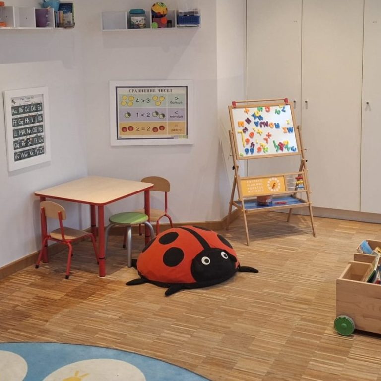 Bunte Kinderecke mit Tisch, Stühlen, einer Käfer-Kissen und einer Tafel.