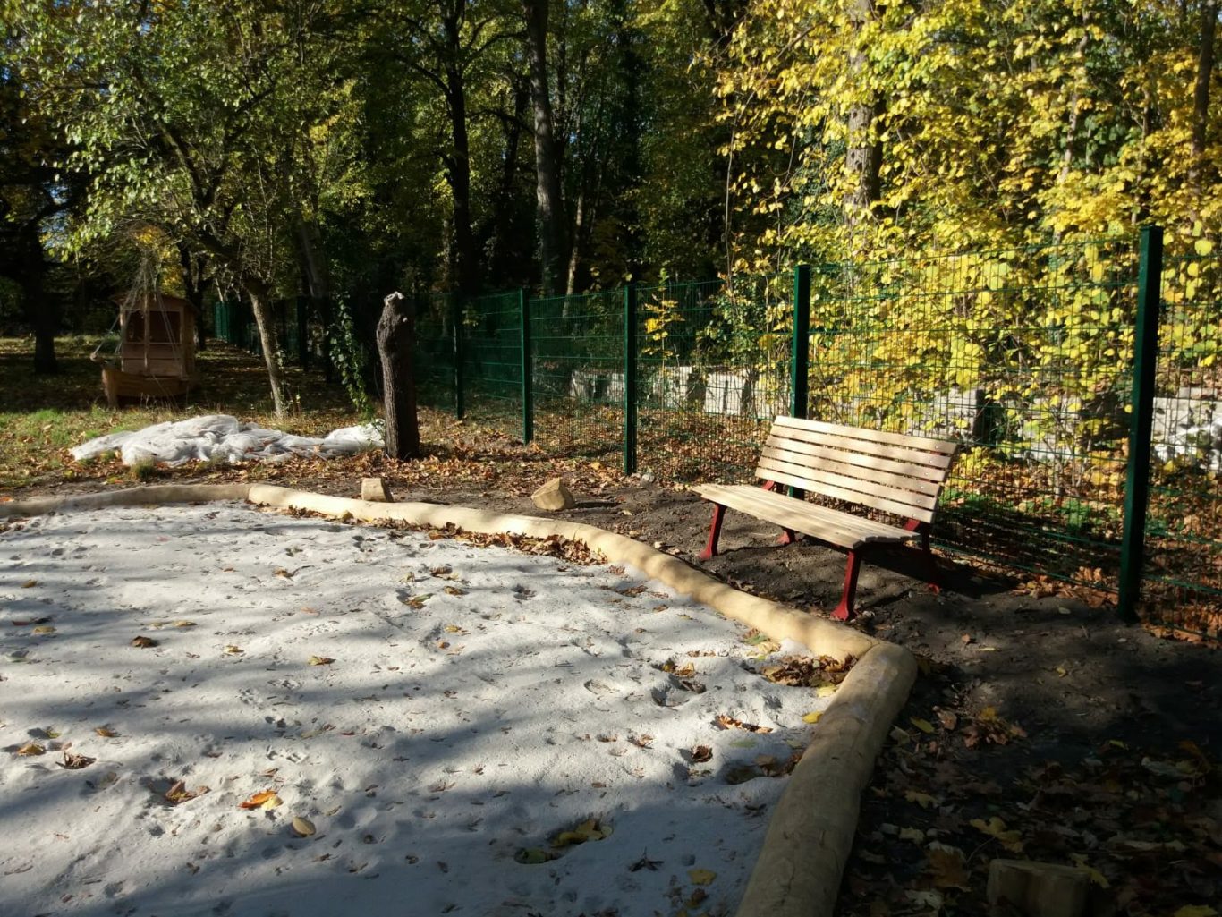 Holzbank in einem Waldgebiet mit Laubbäumen und einem Sandkasten.